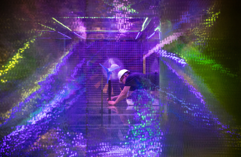 A young man in a hard hat and safety glasses adjusts a small wind turbine inside a wind tunnel.