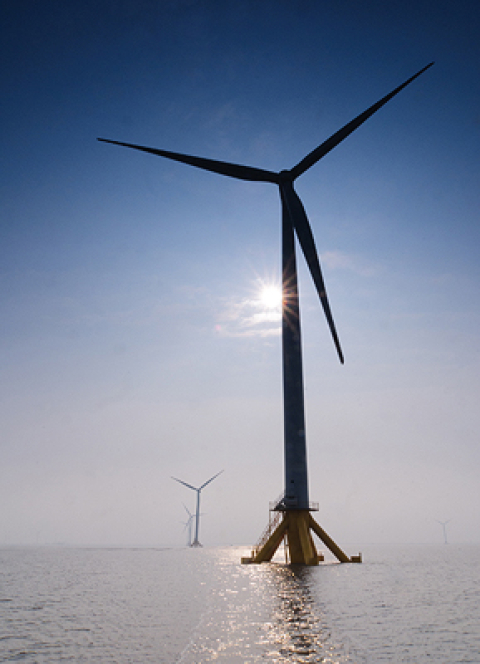 Offshore wind turbines at sea with sun shining.