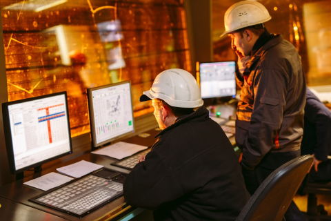 a photo of 2 people working in a control room.