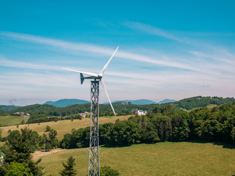 A 15-kilowatt distributed wind turbine stands in a field near a house, with a blue sky in the background.