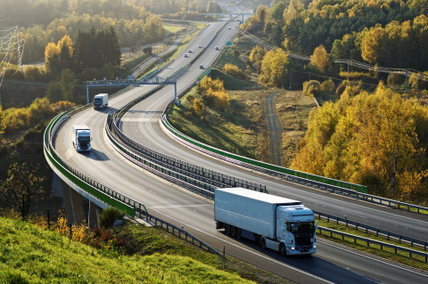 Image of trucks traveling down a long road in the fall