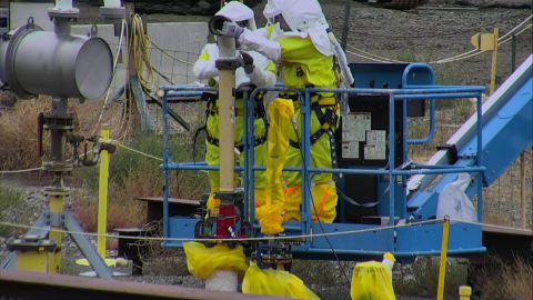Workers at the Hanford Site make final connections between a pipe sticking up out of one of three aging underground structures being stabilized and a grout delivery system.