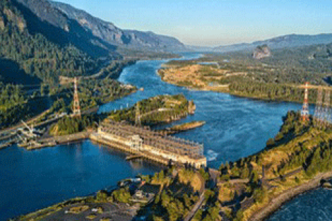 A photo of a water power statin on a blue river surrounded by forested hills.