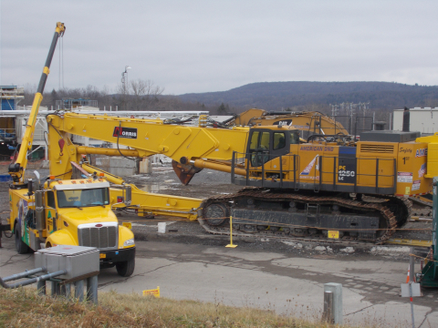 Workers at the West Valley Demonstration Project install a long-reach arm on a large excavator that will be used for the demolition of the Main Plant Process Building.