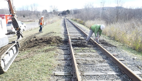 Using a small excavator, workers replace railroad ties along a track within the West Valley Demonstration Project used to ship waste offsite for disposal. 