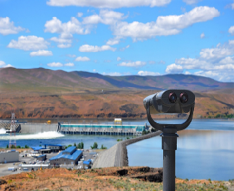 A dam on a river as seen from behind a viewing machine positioned on a hill nearby.