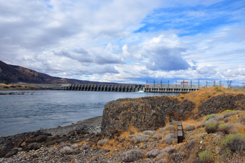 View of a dam on a river from a rocky shoreline.