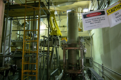 A robotic arm, shown in yellow at center, undergoes testing at the Integrated Waste Treatment Unit at DOE's Idaho National Laboratory Site to remove contamination from stainless steel canisters containing a treated waste product. 