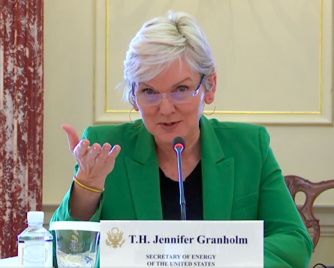Secretary Jennifer Granholm sits at a table wearing a black shirt and a green blazer as she addresses the public and other representatives at the U.S.-EU Energy Council meeting on Monday, Feb. 7, 2022.
