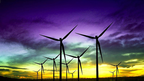 Wind turbines against a yellow, green and purple sky.