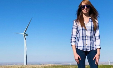Lindsay Sheridan stands in a wind farm on a clear day.