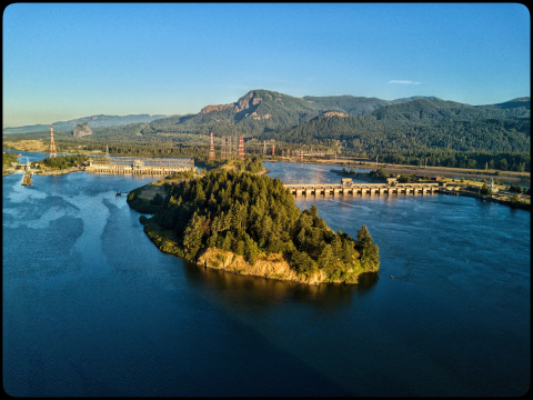 Hydropower dam with greenery surrounding it and mountains in the background.