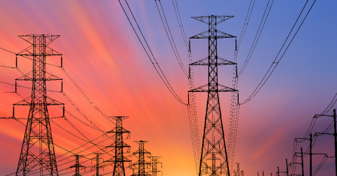Transmission towers and power lines against a backdrop of a multi-colored sky at sunset