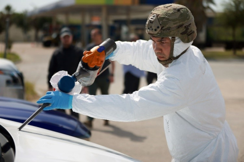 A man in a helmet uses an instrument to collect dust from a car's windshield wiper. He is wearing a military-style helmet.