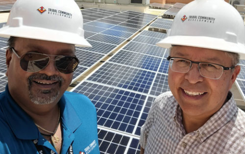 Two men with hard hats pose with roof top solar panels.