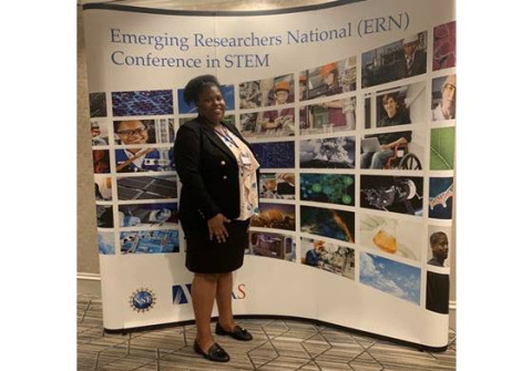 Lauri Kight standing in front of a sign with photos and text: "Emerging Researchers National (ERN) Conference in STEM"