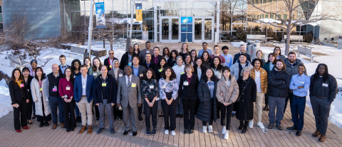 A group of people standing outside the entrance of a large building, facing the camera.