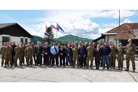 A large group of people pose for a photo outside with Slovenian flag flying behind them.