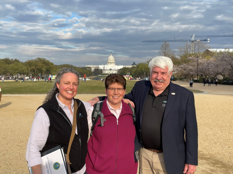 three people pose in front of the United States Capitol building