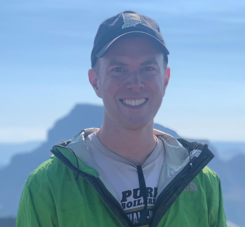 A man stands in front of mountains and smiles. 