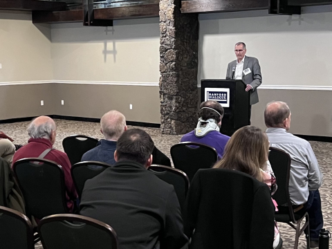A man stands at a podium at the front of a room while the audience looks at him