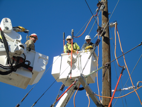 Workers in cherry pickers working near telephone pole.