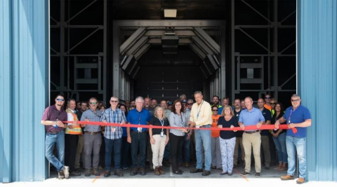 A large group of people pose for a picture while performing a ribbon cutting