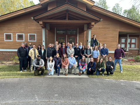 A large group of people pose for a photo in front of a brown building