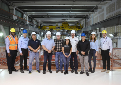  A group of Washington state leaders wearing hard hats and pose for a picture inside a facility building 