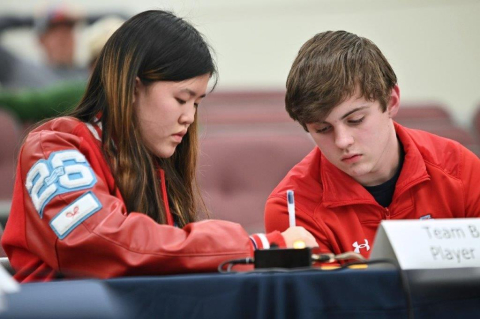Two high school students sitting at a table, one is writing while the other watches