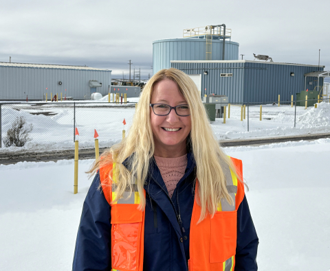 A woman in an orange work vest in front of a large facility building