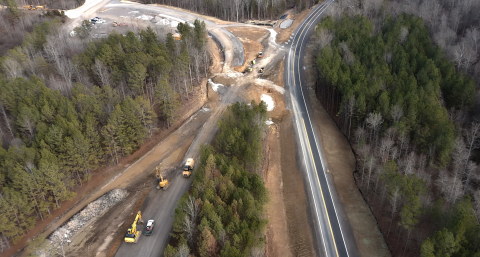 Aerial view of two long roads with trucks and cars on them surrounded by lots of trees