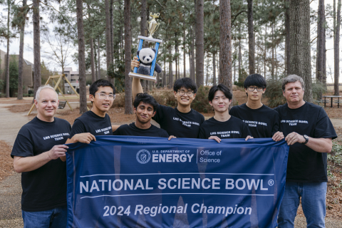A group of high school students and their coaches hold up a winners banner
