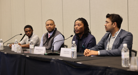 A group of individuals sitting at a table speaking into microphones during a panel 