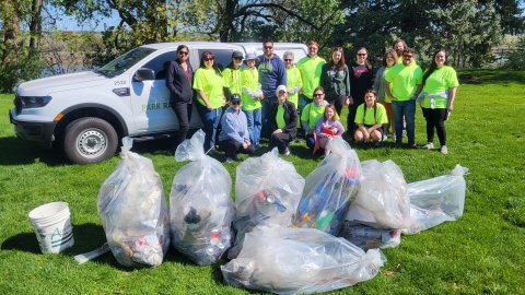 Group photo outside with people standing in front of filled trash bags. 
