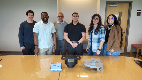 A group of college students pose for a picture while standing in front of a table
