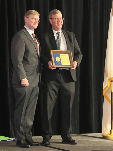 Two men posing for a picture, one holding an award plaque
