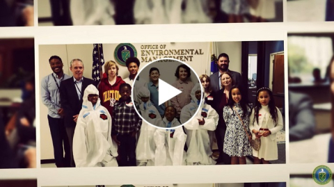 Play button over a still from a YouTube video with a group picture of adults and kids, some in hazmat suits