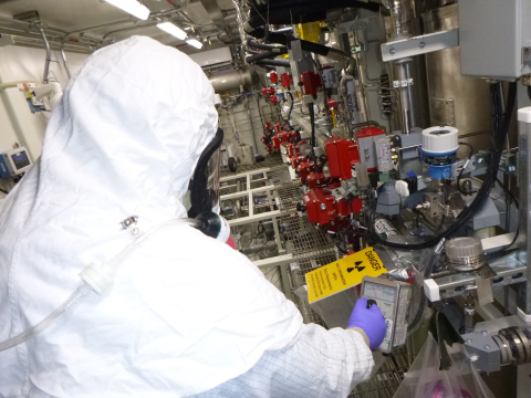 An employee in a white hazmat suit works on a machine with a yellow danger sign on it 