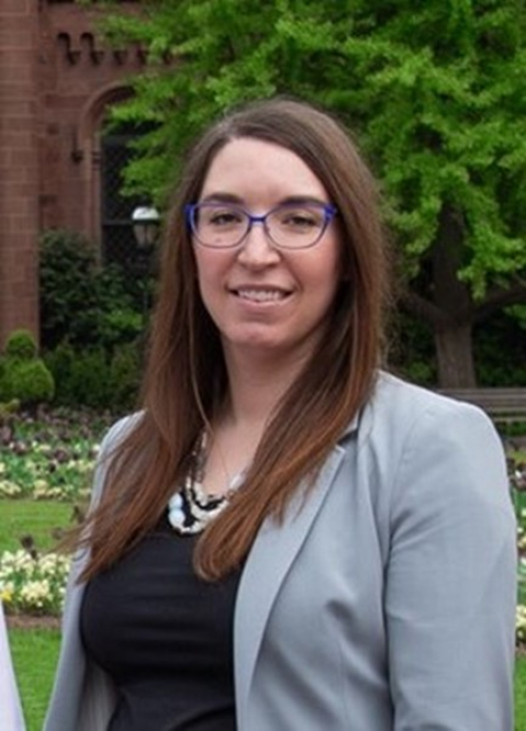 Headshot of a woman with brown hair, glasses, and a gray blazer