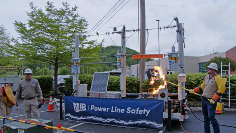 Professionals performing a safety demonstration, one man holds an object on fire while the other explains what is going on 