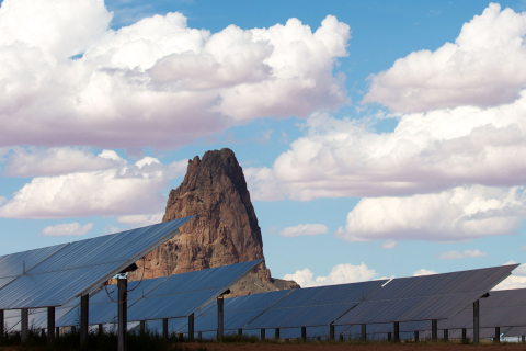 Solar panels with desert rock formation in background.