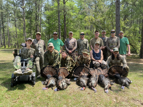 Group photo of hunters dressed in camouflage, some holding turkeys that they hunted 