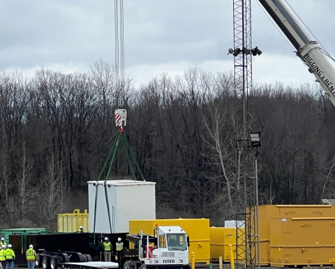 A crane loads large containers of waste onto a truck