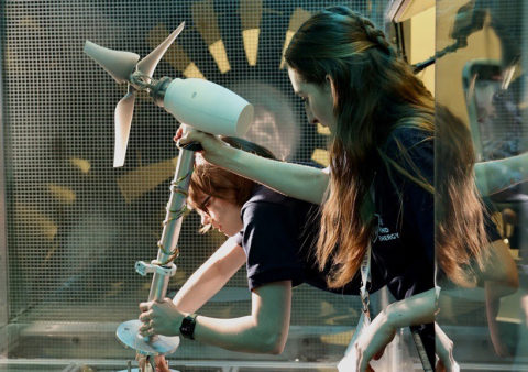 Two people setting up a wind turbine prototype inside of a wind tunnel