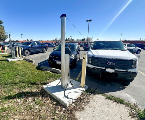 A parking lot full of vehicles with two up-close vehicles plugged into an electric vehicle charging station