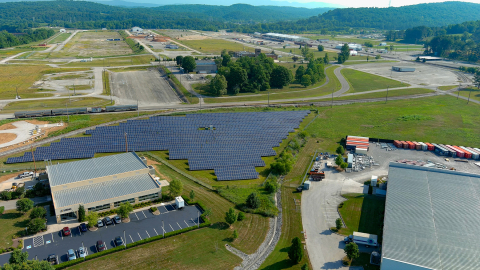 Aerial shot of land with two buildings and many rows of solar panels on it 