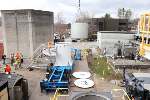 An overhead shot of a waste tank being lifted onto a shipping truck with workers around