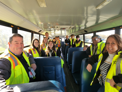 A group of people wearing yellow safety vests sit on a school bus and face toward the camera for a picture