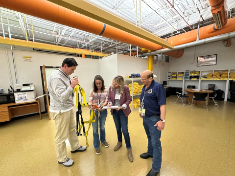 A group of four people stand inside a training facility room and look at a piece of paper together